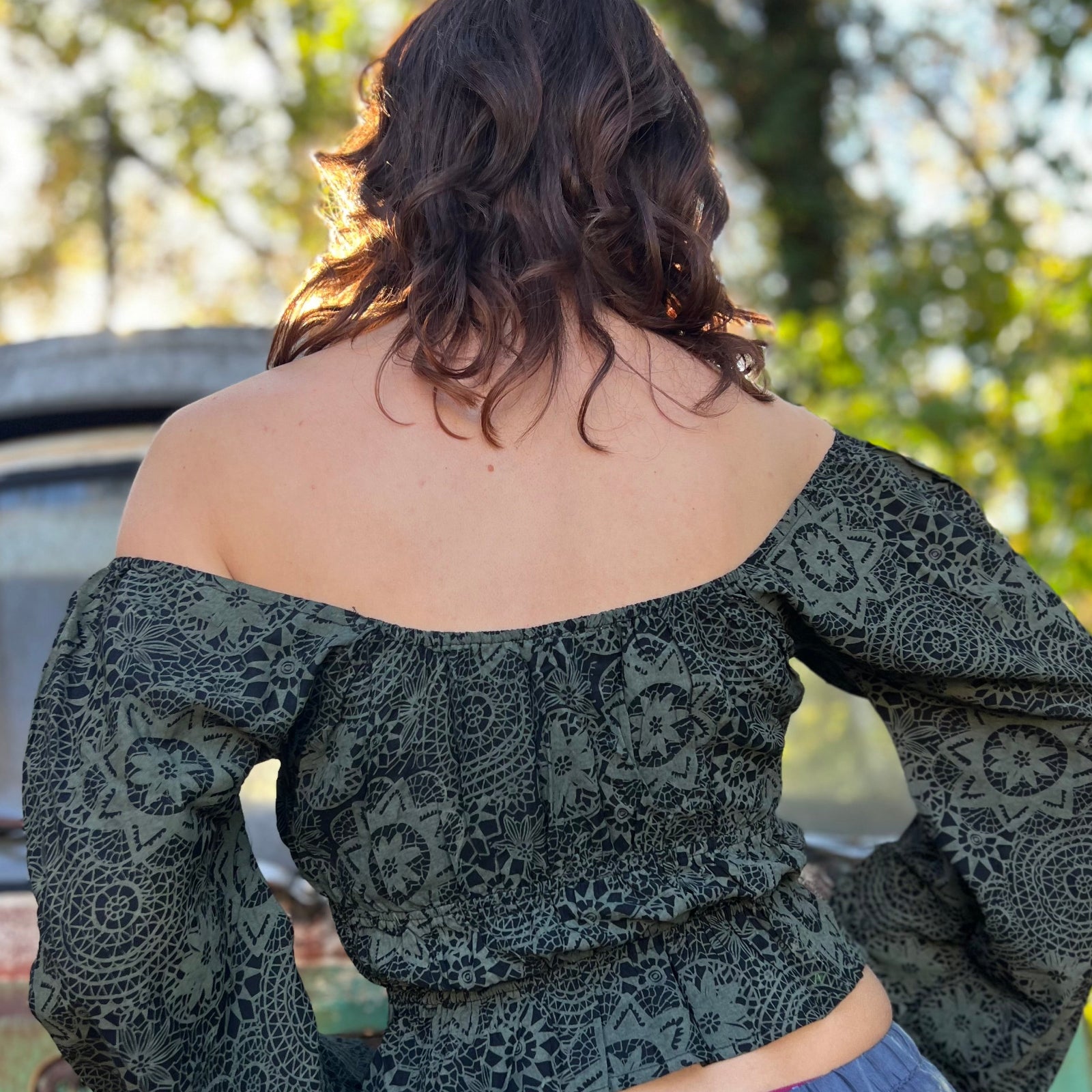 A woman wearing the forest Flowy Peasant Viscose Print Blouse with a skirt in front of the vintage teal Volkswagen bus, showing off the back.