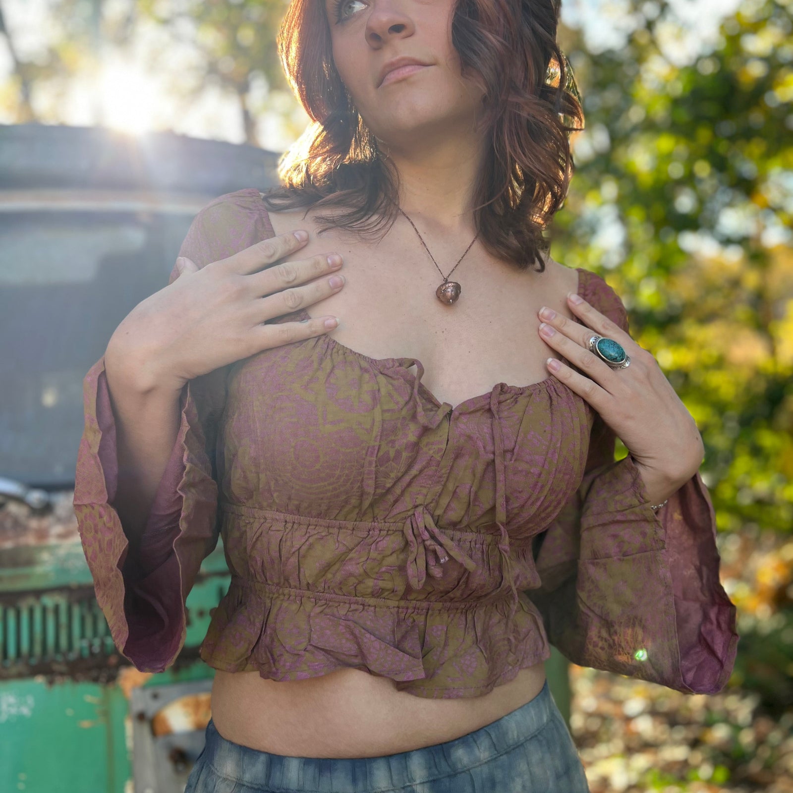 A woman wearing the maroon Flowy Peasant Viscose Print Blouse with a skirt in front of the vintage teal Volkswagen bus.