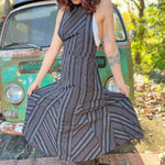 A woman wearing the black Striped Twirl Skirt Cotton Overall with brown boots in front of a vintage teal Volkswagen bus.