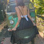 A woman wearing the black Striped Twirl Skirt Cotton Overall with brown boots in front of a vintage teal Volkswagen bus.