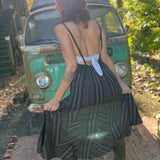 A woman wearing the black Striped Twirl Skirt Cotton Overall with brown boots in front of a vintage teal Volkswagen bus.