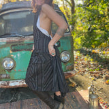 A woman wearing the black Striped Twirl Skirt Cotton Overall with brown boots in front of a vintage teal Volkswagen bus.