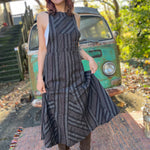 A woman wearing the black Striped Twirl Skirt Cotton Overall with brown boots in front of a vintage teal Volkswagen bus.
