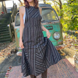 A woman wearing the black Striped Twirl Skirt Cotton Overall with brown boots in front of a vintage teal Volkswagen bus.