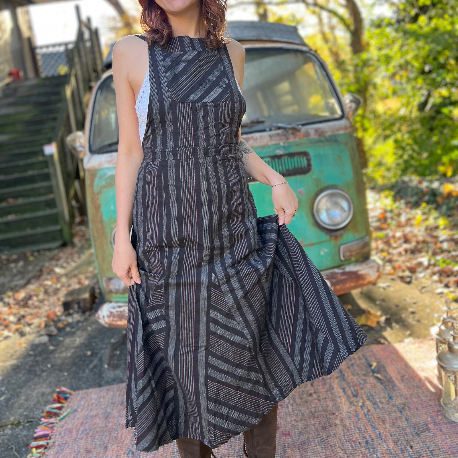 A woman wearing the black Striped Twirl Skirt Cotton Overall with brown boots in front of a vintage teal Volkswagen bus.