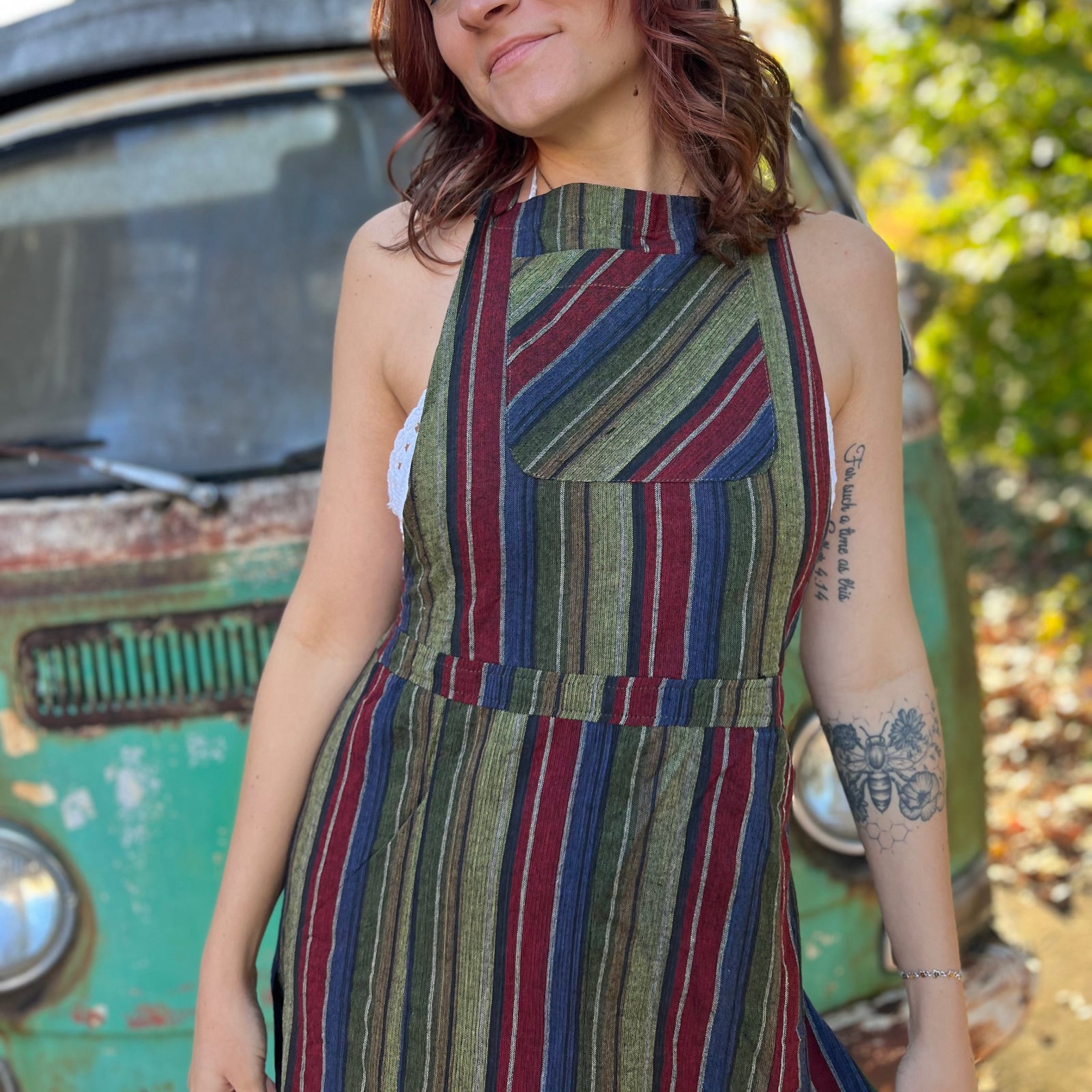 A woman wearing the olive Striped Twirl Skirt Cotton Overall with brown boots in front of a vintage teal Volkswagen bus.