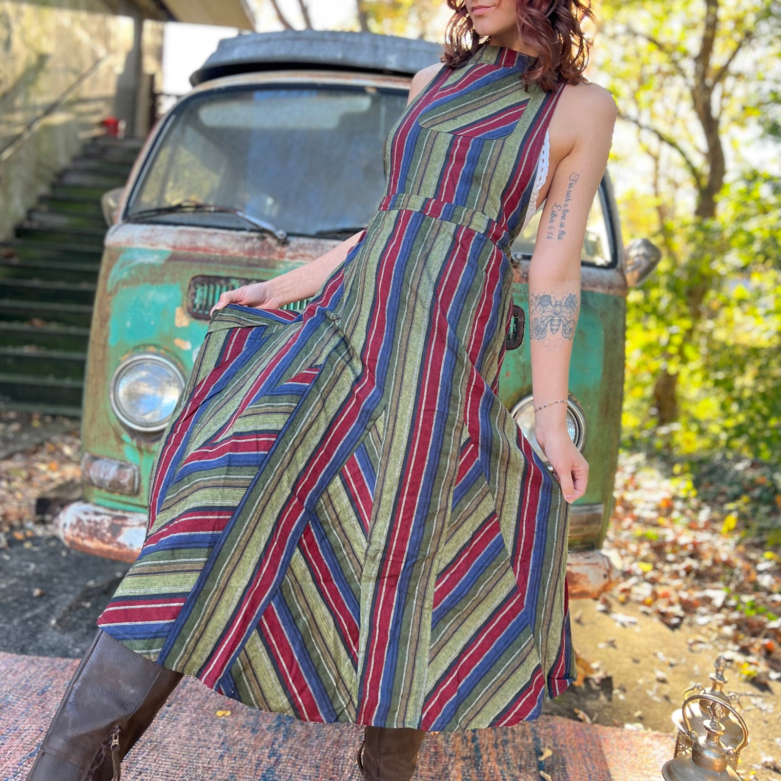 A woman wearing the olive Striped Twirl Skirt Cotton Overall with brown boots in front of a vintage teal Volkswagen bus.