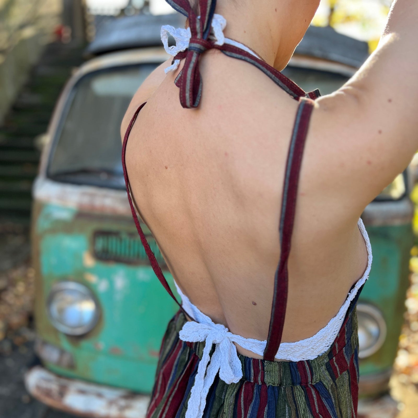 A woman wearing the olive Striped Twirl Skirt Cotton Overall with brown boots in front of a vintage teal Volkswagen bus., showing off the back.