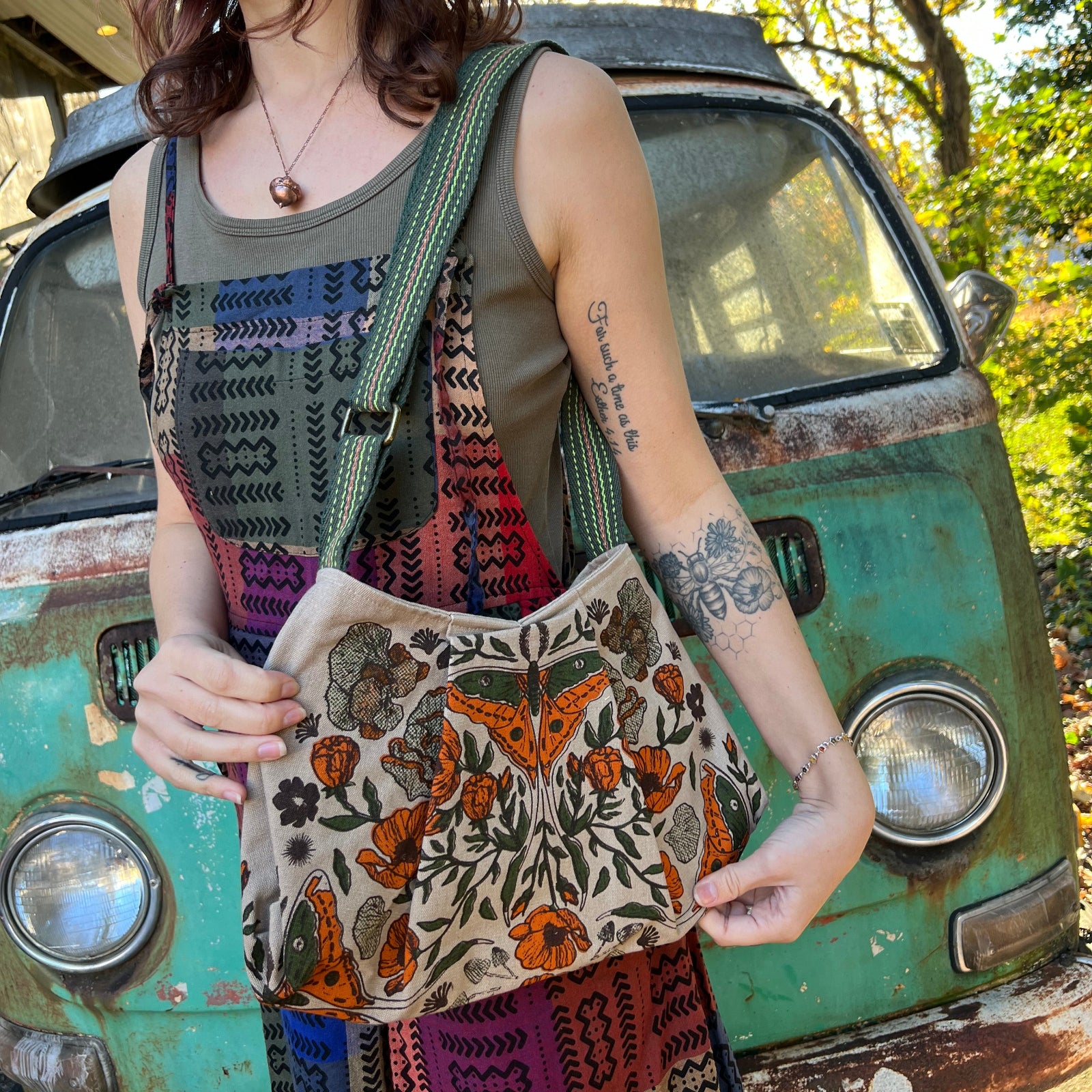 A woman in a hippie jumpsuit wearing the Luna Moth Print Cotton Bag.