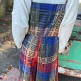 A woman wearing the Cotton Plaid Wide Leg Overalls with a white long sleeve in front of a vintage teal Volkswagen bus, showing off the back.