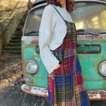 A woman wearing the Cotton Plaid Wide Leg Overalls with a white long sleeve in front of a vintage teal Volkswagen bus, showing off the side.