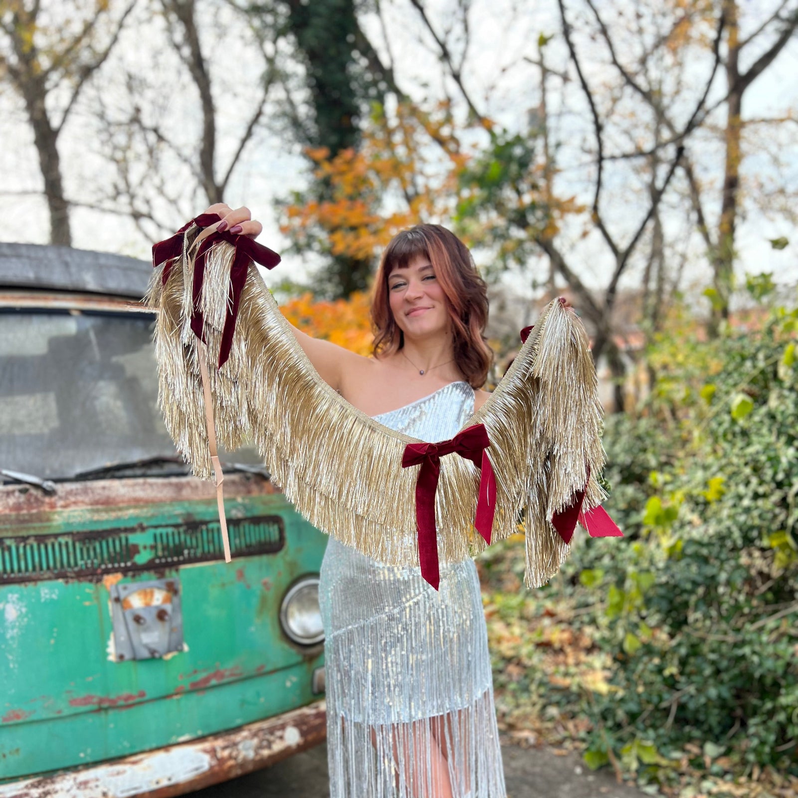 Someone holding the Gilded Bow Gold Layered Fringe Banner in front of a vintage teal Volkswagen bus.