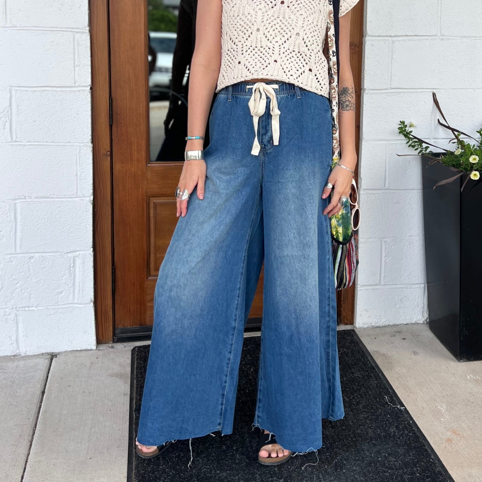 A woman wearing the dark wash Denim Drawstring Waist Band Wide Leg Pants with a cream crocheted top.