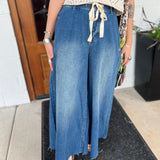 A woman wearing the dark wash Denim Drawstring Waist Band Wide Leg Pants with a cream crocheted top.