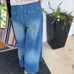 A woman wearing the dark wash Denim Drawstring Waist Band Wide Leg Pants with a cream crocheted top.