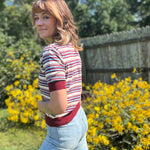 A woman wearing the Striped Knit Sweater Half Button Up Collar Top with some jeans on, in front of some greenery.