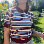 A woman wearing the Striped Knit Sweater Half Button Up Collar Top with some jeans on, in front of some greenery.