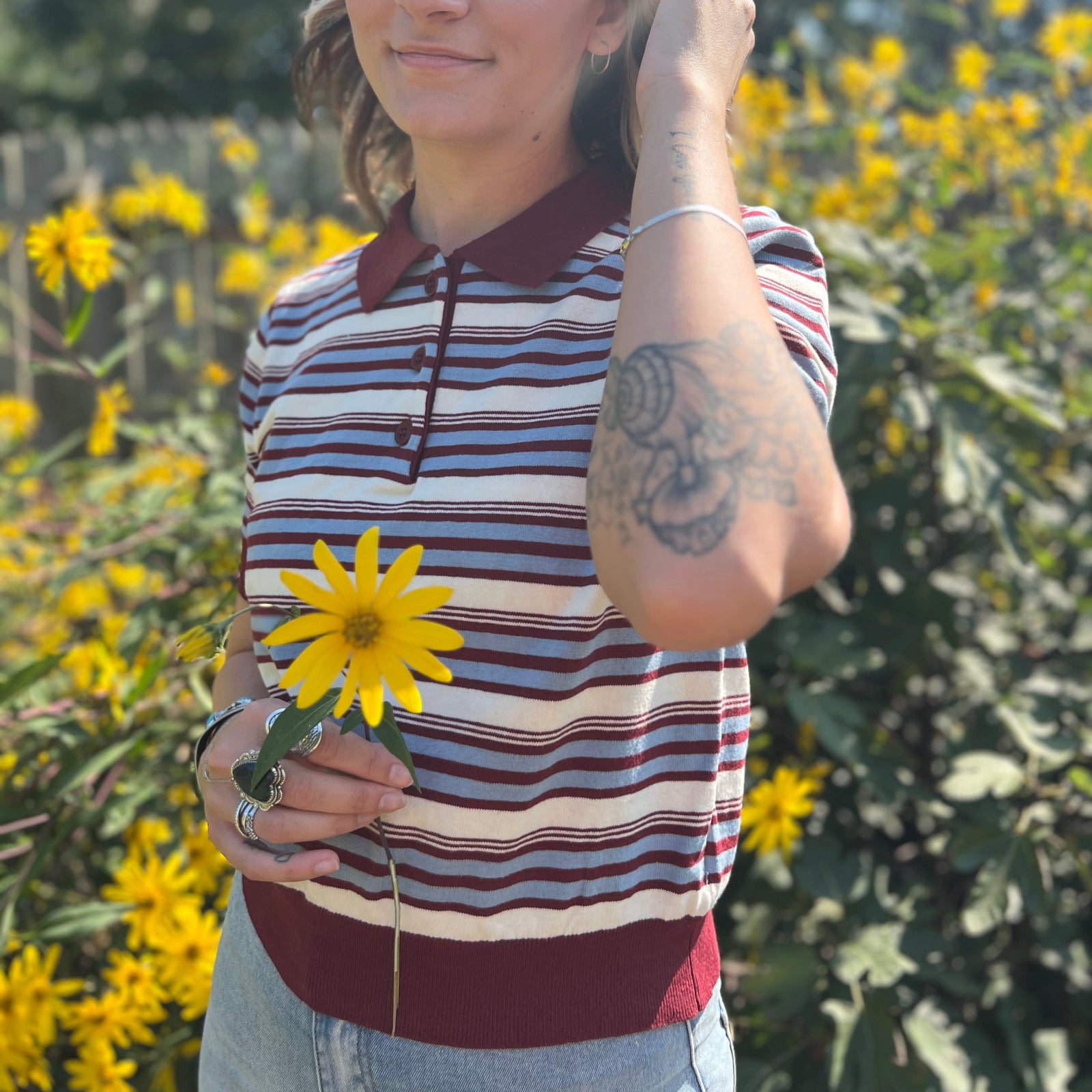 A woman wearing the Striped Knit Sweater Half Button Up Collar Top with some jeans on, in front of some greenery.