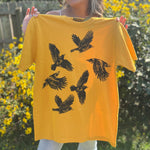 A woman holding the Crows Organic Cotton T Shirt in front of some greenery.
