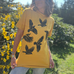 A woman wearing the Crows Organic Cotton T Shirt with some jeans in front of some greenery.