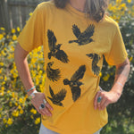 A woman wearing the Crows Organic Cotton T Shirt with some jeans in front of some greenery.