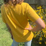 A woman wearing the Crows Organic Cotton T Shirt with some jeans in front of some greenery.