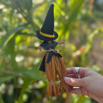 Someone holding a Witch Samhain Folk Corn Husk Poppet Doll in front of greenery, showing off the back.