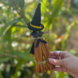 Someone holding a Witch Samhain Folk Corn Husk Poppet Doll in front of greenery, showing off the back.