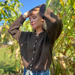 A woman wearing the dark chocolate Knit Round Neck Sweater Cardigan Top with jeans in front of some greenery.