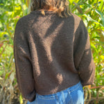 A woman wearing the dark chocolate Knit Round Neck Sweater Cardigan Top with jeans in front of some greenery.