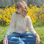 A woman sitting down and wearing the Beige Knit Nylon Wool Spandex Sweater with jeans in front of yellow flowers.