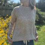 A woman wearing the Beige Knit Nylon Wool Spandex Sweater with jeans in front of yellow flowers.