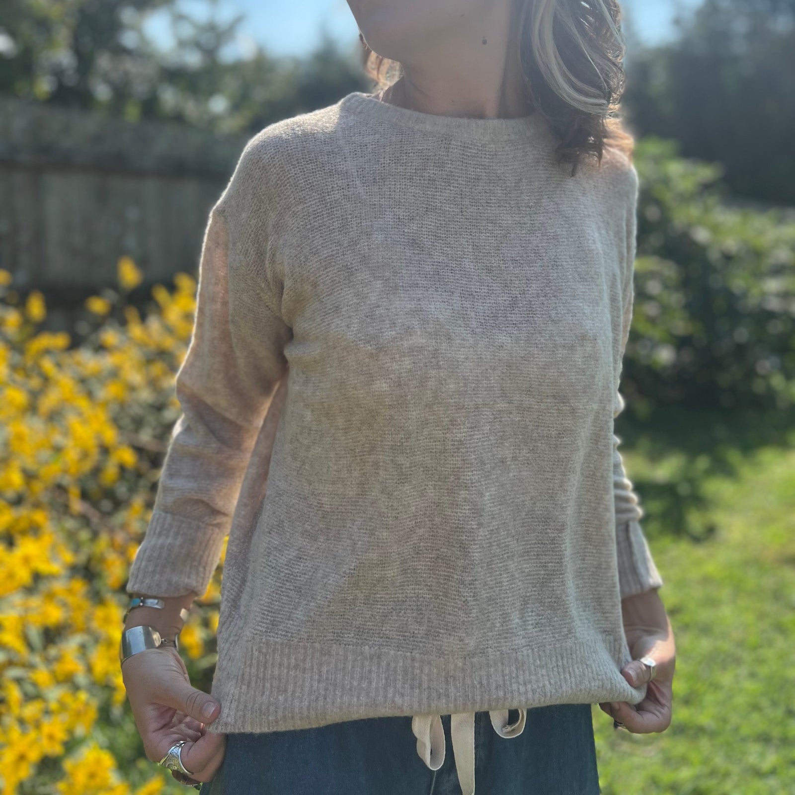 A woman wearing the Beige Knit Nylon Wool Spandex Sweater with jeans in front of yellow flowers.