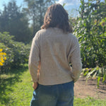 A woman wearing the Beige Knit Nylon Wool Spandex Sweater with jeans in front of yellow flowers.