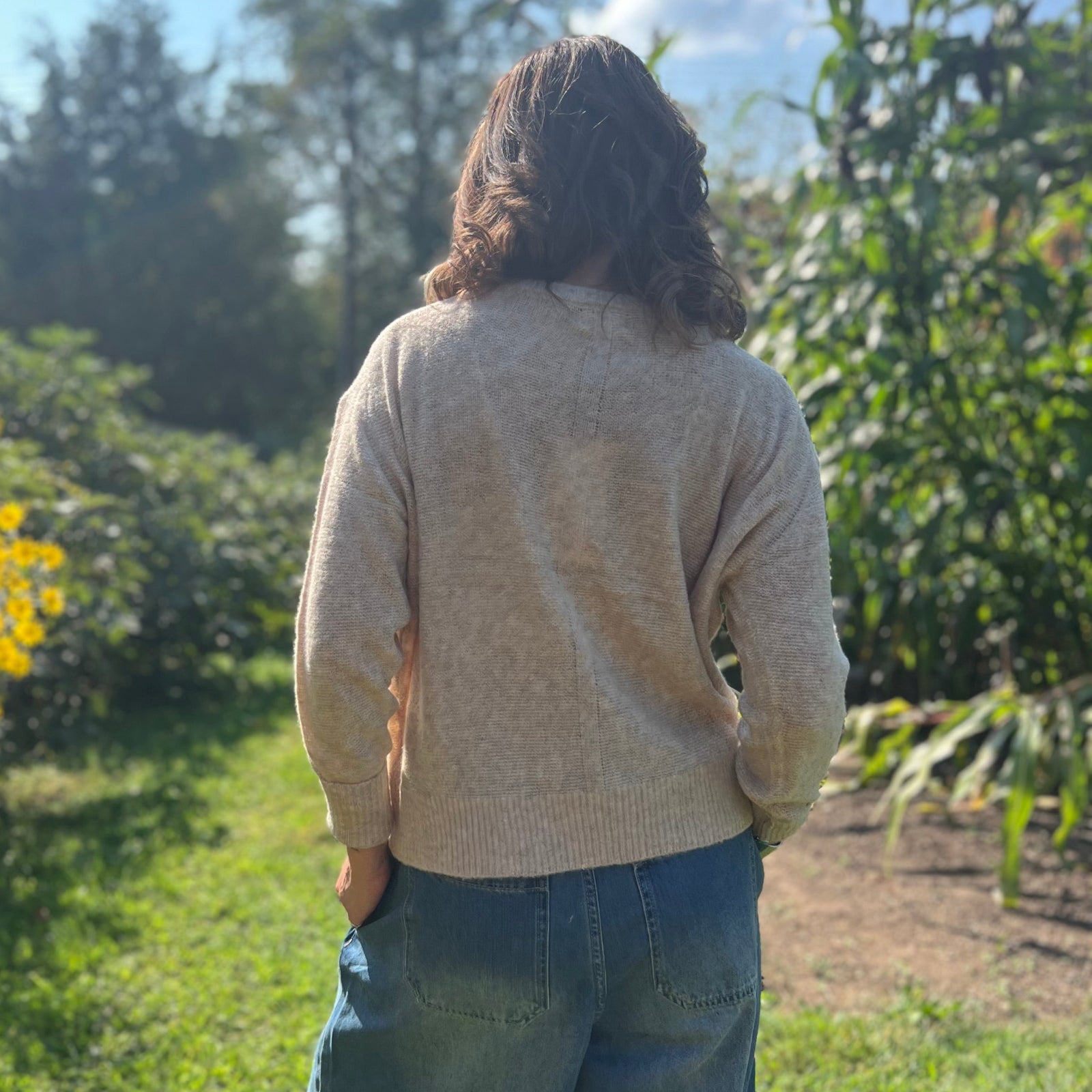 A woman wearing the Beige Knit Nylon Wool Spandex Sweater with jeans in front of yellow flowers.