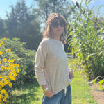 A woman wearing the Beige Knit Nylon Wool Spandex Sweater with jeans in front of yellow flowers.