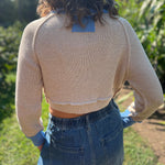 A woman wearing the Contrast Knitted Crew Neck Button Down Cardigan Sweater with denim pants in front of greenery, showing off the back.