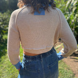 A woman wearing the Contrast Knitted Crew Neck Button Down Cardigan Sweater with denim pants in front of greenery, showing off the back.