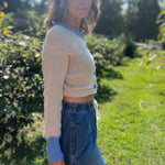 A woman wearing the Contrast Knitted Crew Neck Button Down Cardigan Sweater with denim pants in front of greenery, showing off the side.