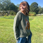 A woman wearing the Horse Embroidery Knit Pullover Sweater with the denim pants, showing off the side.