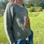 A woman wearing the Horse Embroidery Knit Pullover Sweater with the denim pants, showing off the side.
