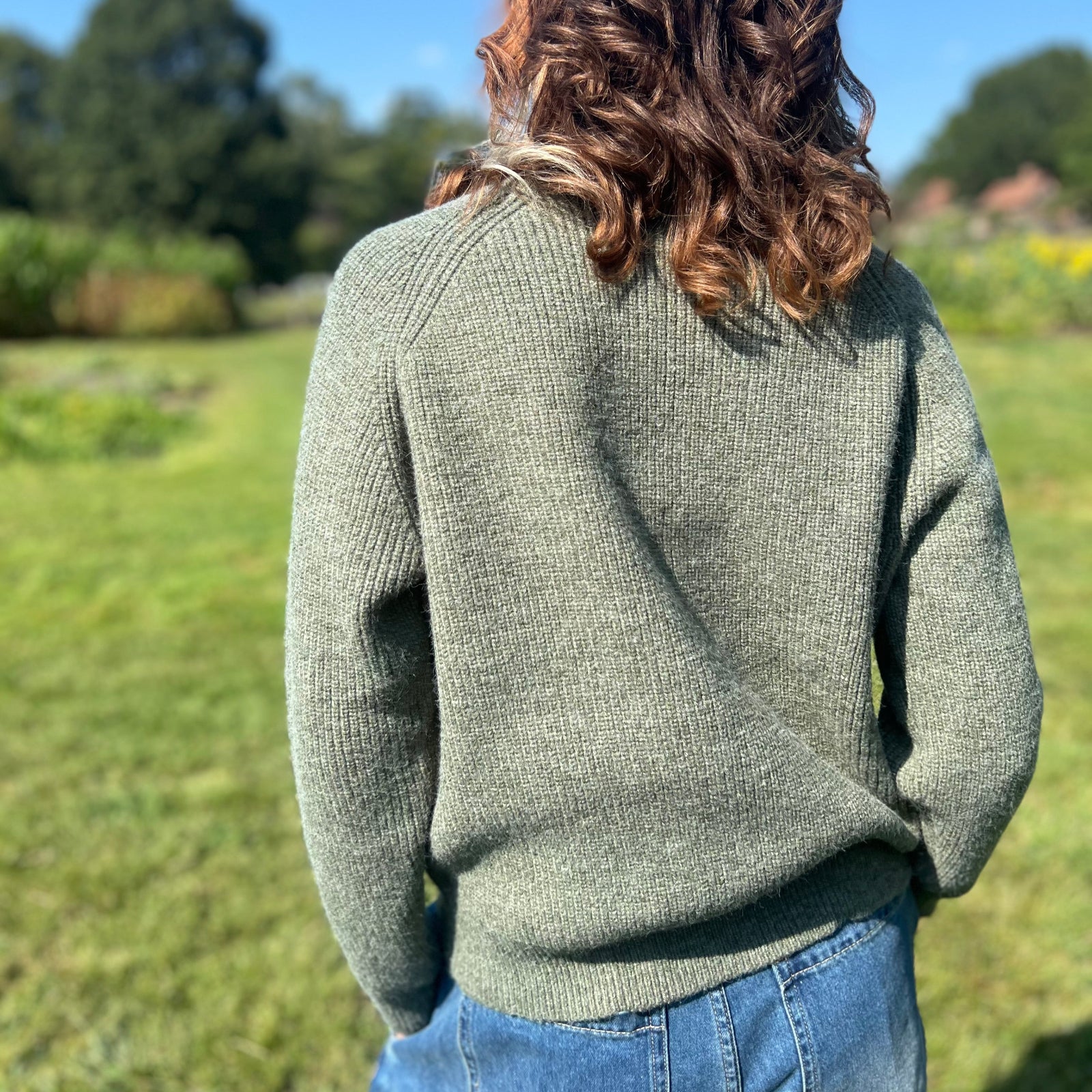 A woman wearing the Horse Embroidery Knit Pullover Sweater with the denim pants, showing off the back.