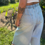 A woman wearing the light wash Denim Drawstring Waist Band Wide Leg Pants with a cream crocheted top.