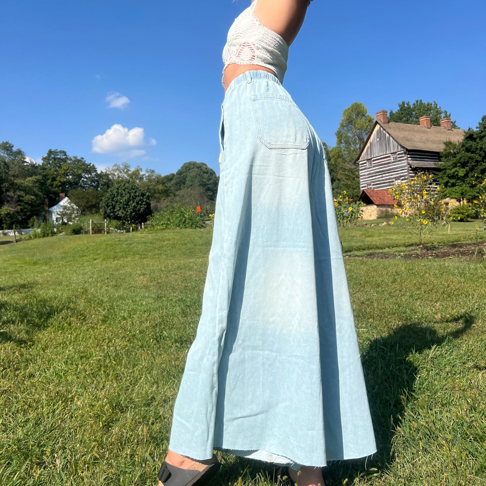 A woman wearing the light wash Denim Drawstring Waist Band Wide Leg Pants with a cream crocheted top.