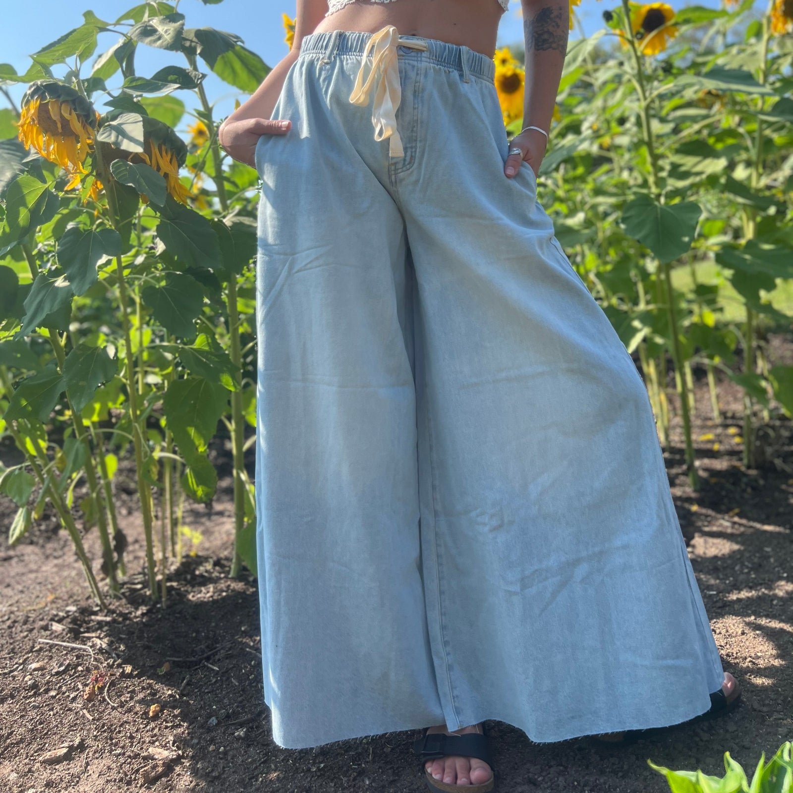 A woman wearing the light wash Denim Drawstring Waist Band Wide Leg Pants with a cream crocheted top.