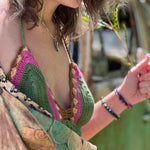 A woman wearing the sage Festive Crochet Top: One Size with patchwork overalls and an evil eye necklace.