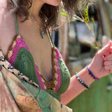 A woman wearing the sage Festive Crochet Top: One Size with patchwork overalls and an evil eye necklace.