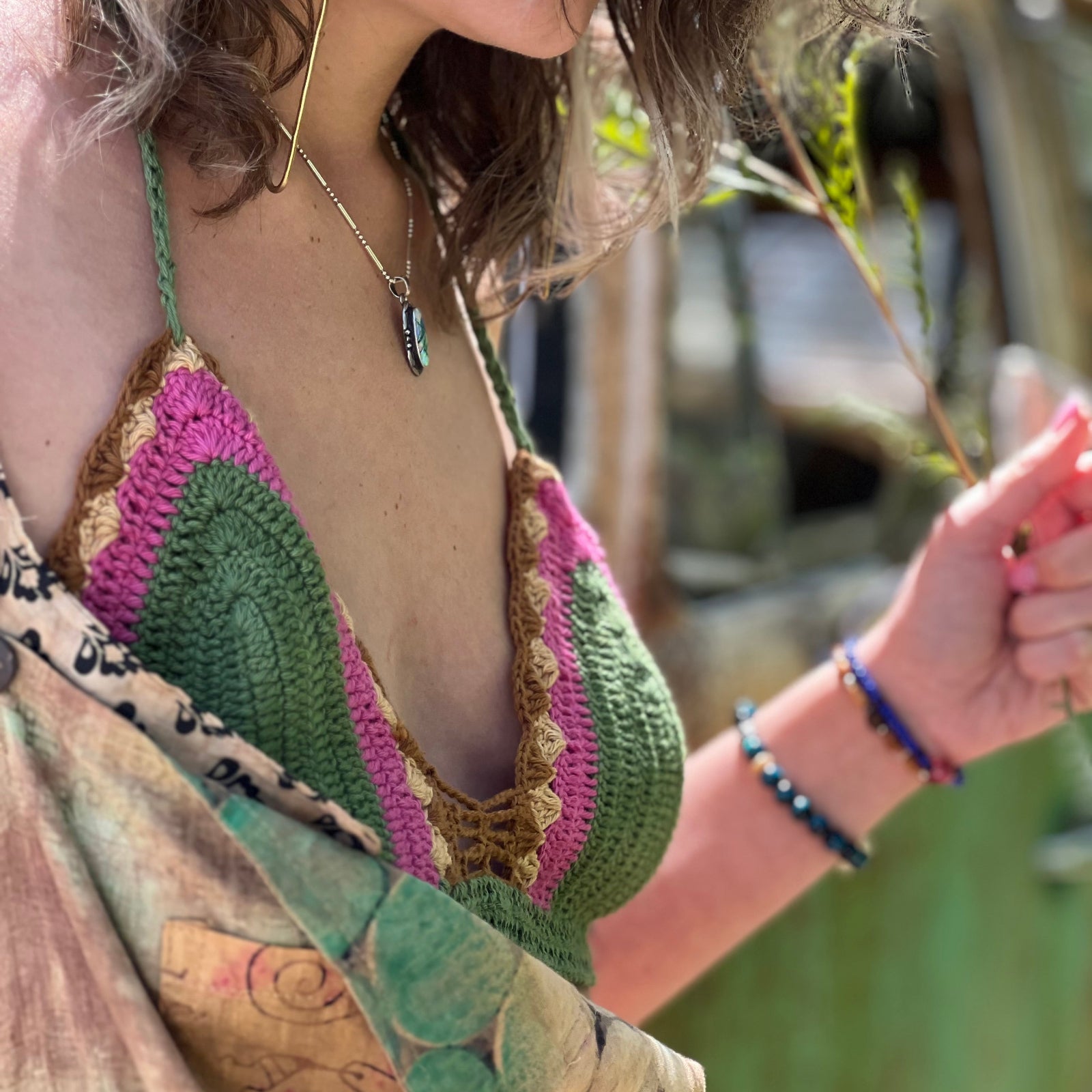 A woman wearing the sage Festive Crochet Top: One Size with patchwork overalls and an evil eye necklace.