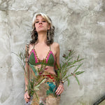 A woman wearing the sage Festive Crochet Top: One Size with patchwork overalls and an evil eye necklace.