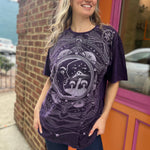 A woman wearing the Purple Mushroom Stonewashed Cotton T-shirt with jeans in front of a pink and orange wall.